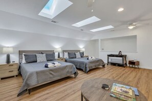 A modern bedroom with two beds, a desk, and a ceiling fan.