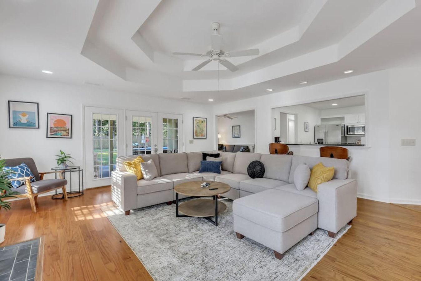 A spacious living room with a large sectional sofa, a coffee table, and a dining area with a kitchen in the background.