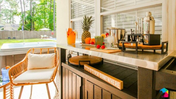 A kitchen with a bar area, a wicker chair, and a sign that says "IT'S 5 O'CLOCK SOMEWHERE". - Savannah 5BR Pool, Jacuzzi, Firepit, Sports, Games (Savannah)