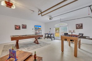 A room with a foosball table, pool table, and a television on the wall.