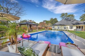 A backyard with a swimming pool, lounge chairs, and a covered patio area.
