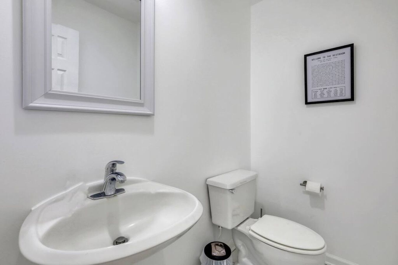 A bathroom with a white sink, toilet, and a framed sign on the wall.