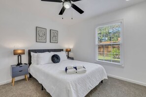 A bedroom with a bed, two bedside tables, a ceiling fan, and a window with blinds.