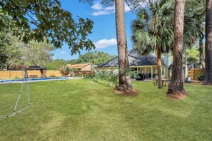 A backyard with a swimming pool, a covered patio, and a lawn.