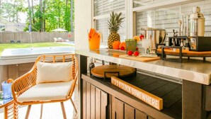 A kitchen with a bar area, a wicker chair, and a sign that says "IT'S 5 O'CLOCK SOMEWHERE". - Savannah 5BR Pool, Jacuzzi, Firepit, Sports, Games (Savannah)