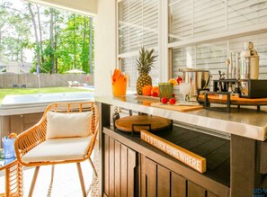 A kitchen with a bar area, a wicker chair, and a sign that says "IT'S 5 O'CLOCK SOMEWHERE".