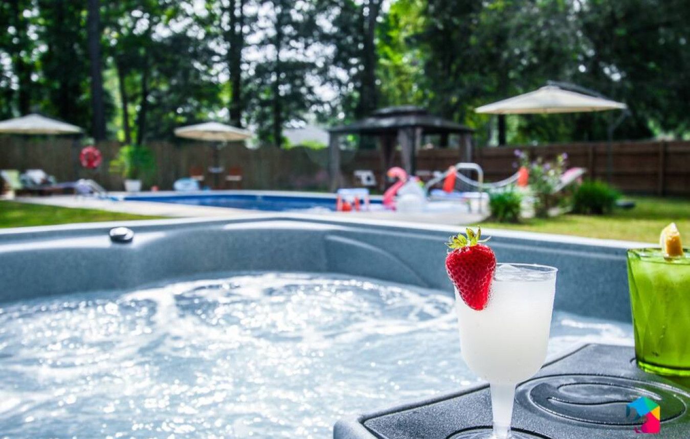 A hot tub with a glass of a white beverage garnished with a strawberry, surrounded by outdoor furniture and umbrellas.