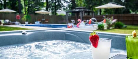 A hot tub with a glass of a white beverage garnished with a strawberry, surrounded by outdoor furniture and umbrellas.