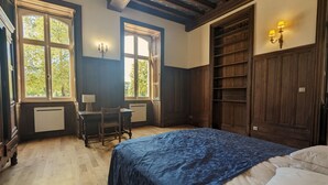 A bedroom with a large bed, two windows, a desk with a chair, and built-in shelving. - Ground Floor Apartment in Historic Setting, Near Downtown Châteauroux (Châteauroux)