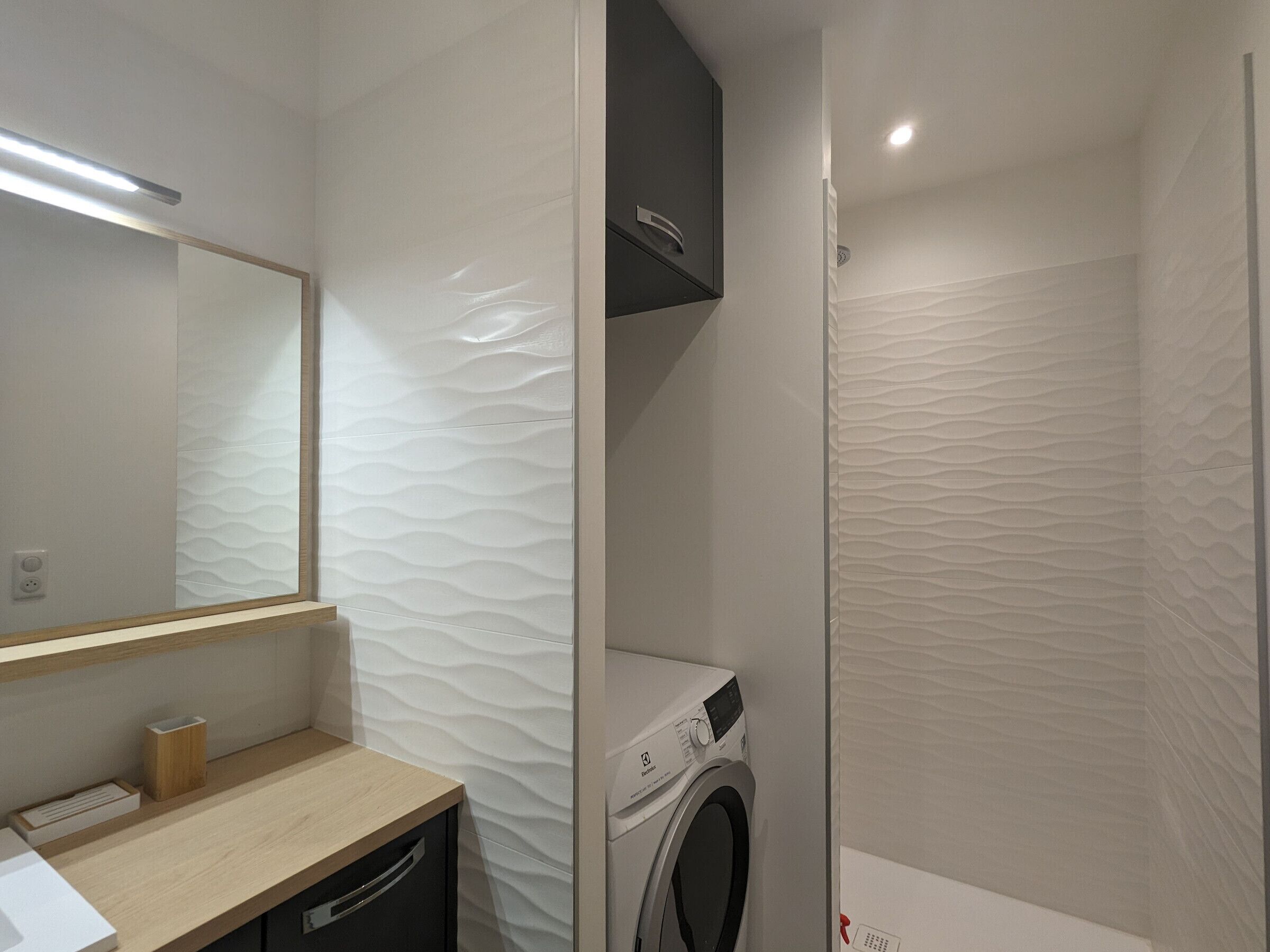 Une salle de bain moderne dotée d’un lave-linge encastré, d’un meuble-lavabo en bois et d’un grand miroir.