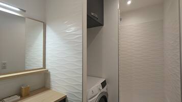 Une salle de bain moderne dotée d’un lave-linge encastré, d’un meuble-lavabo en bois et d’un grand miroir.