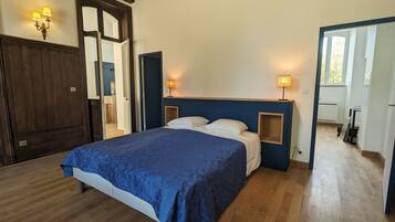 A bedroom with a large bed, wooden wardrobe, and a mirror. There are two bedside lamps and a small table with a lamp.