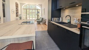 A modern kitchen with dark cabinetry, a wooden island, and a large window providing natural light. - Ground Floor Apartment in Historic Setting, Near Downtown Châteauroux (Châteauroux)