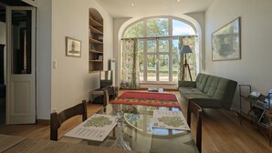 A spacious living room with a glass coffee table, a sofa, and a large window offering a view of greenery. - Ground Floor Apartment in Historic Setting, Near Downtown Châteauroux (Châteauroux)