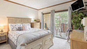 A bedroom with a large bed, a dresser, a TV, and a balcony with a chair and plants. - 3BR Condo Retreat w/ Seasonal Pool & Hot Tub, Balcony, Views & Near Ober Mtn (Gatlinburg)