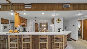 A kitchen with wooden cabinets, a central island with bar stools, and a clock on the wall. - 3BR Condo Retreat w/ Seasonal Pool & Hot Tub, Balcony, Views & Near Ober Mtn (Gatlinburg)