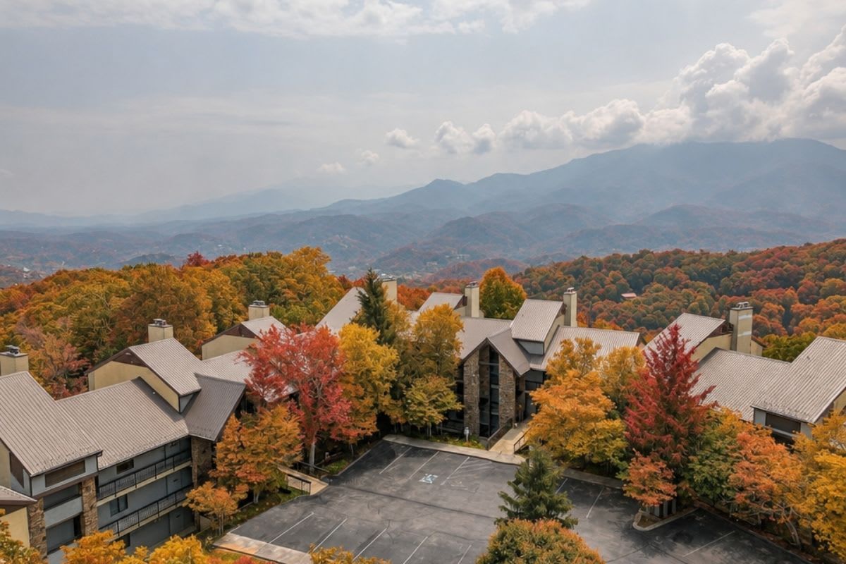 A residential area with multiple buildings surrounded by autumn foliage, a parking lot, and distant mountains.