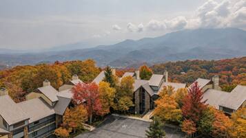 A residential area with multiple buildings surrounded by autumn foliage, a parking lot, and distant mountains.