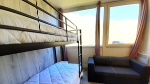 Een kamer met stapelbedden, een slaapbank en een raam met gordijnen.