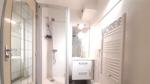Een badkamer met een douche, een spiegel, een wastafel en vloertegels met een patroon.