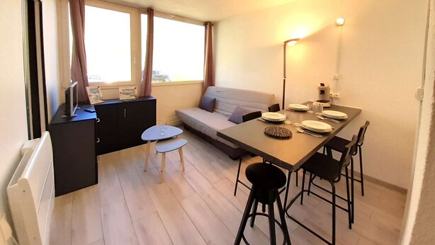 Een knus verblijf met een eettafel, stoelen, een bank, een klein bijzettafeltje en een radiator.