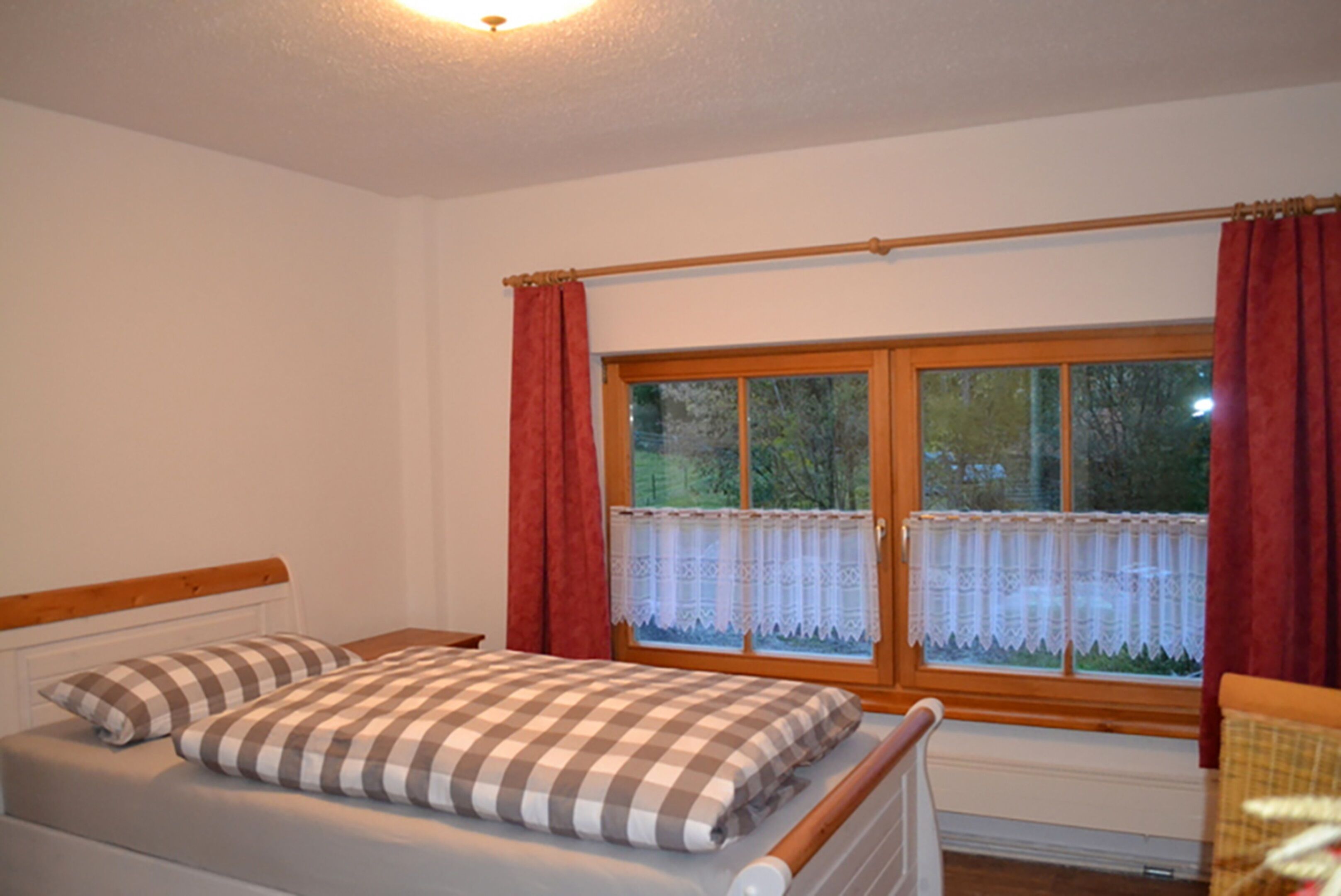 A bedroom with a bed, a window with curtains, and a radiator.