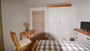 A bedroom with a bed, a chair, a small table with a vase, a wardrobe, and a television on a dresser. - Holzhammer Hof (Bayerbach)