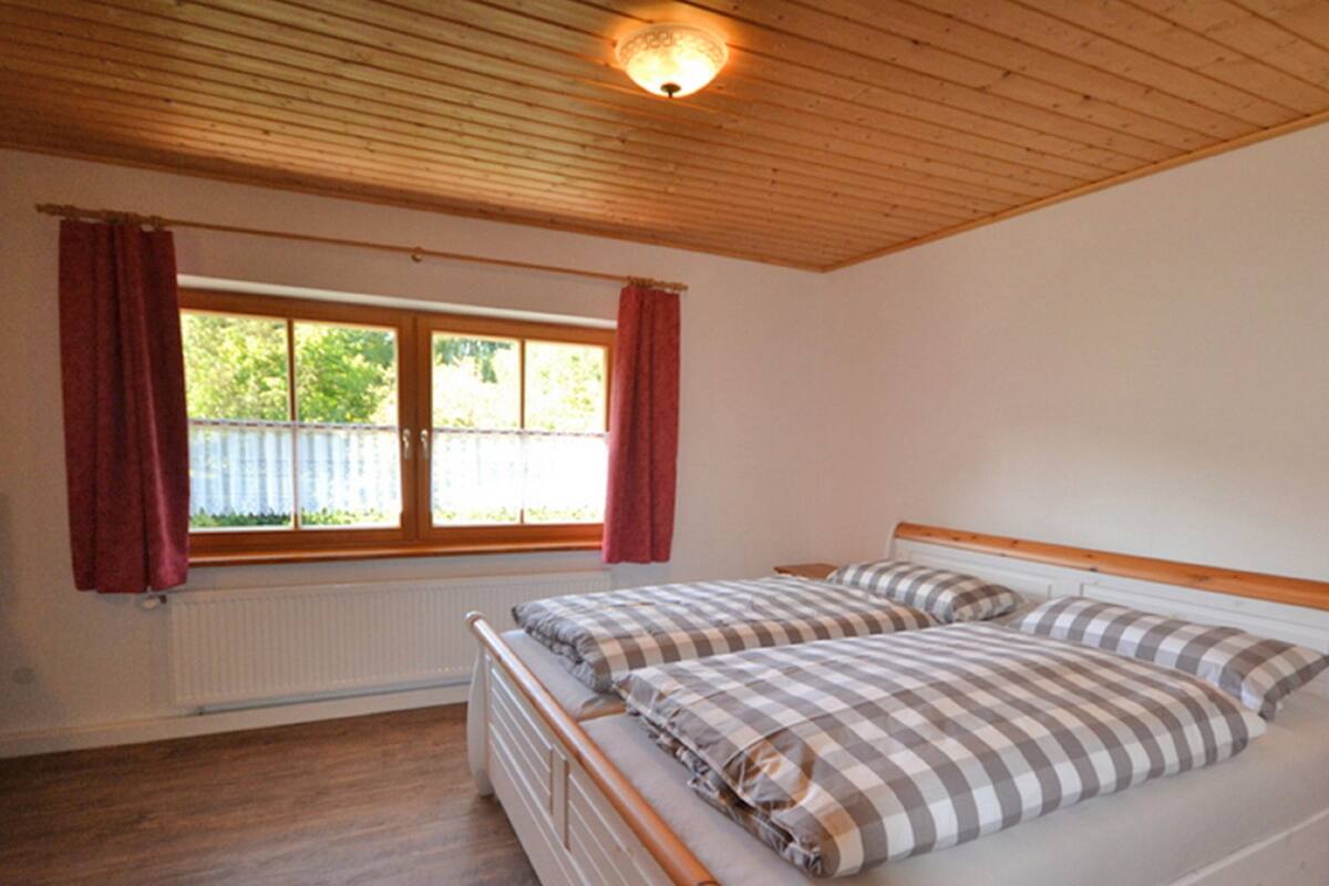 A bedroom with two beds, wooden ceiling, a window with curtains, and a radiator.