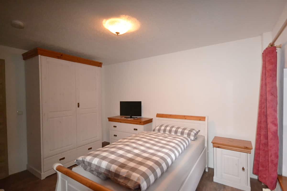 A bedroom with a bed, a TV on a dresser, a wardrobe, and a red curtain.