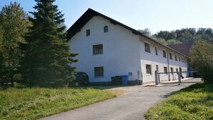 A white building with a sloped roof, a paved driveway, and a small parking area. - Holzhammer Hof (Bayerbach)