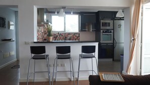 A modern kitchen with a central island, bar stools, and a dining area with a sofa. - Modern House in Bajamar (Bajamar)