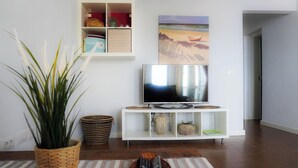 A living room with a TV on a white stand, a potted plant, a striped rug, and a painting on the wall. - Modern House in Bajamar (Bajamar)