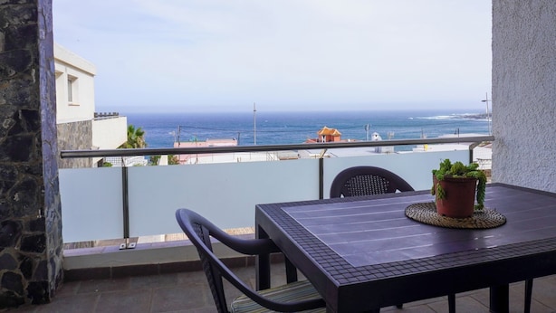A balcony with a view of the sea, a table with chairs, and a potted plant. - Modern House in Bajamar (Bajamar)