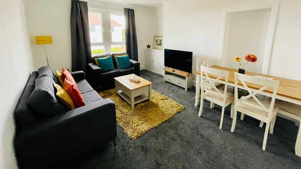 Een moderne woonkamer met een bank, salontafel, televisie en een eethoek.