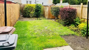Een achtertuin met grasveld, een houten tuinhuis en een hoge boom.