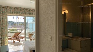 A hotel room with a balcony, a bed, a small table, and a bathroom with a mirror and sink.