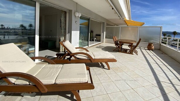 A balcony with sun loungers and a table, large windows, and a view of the sea.