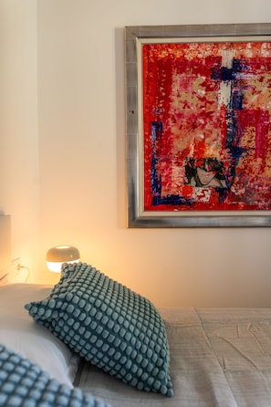 A room with a bed, a green textured pillow, and a red abstract painting on the wall.