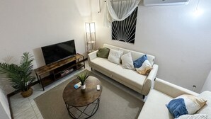 Ein Wohnzimmer mit Fernseher, Sofa, Couchtisch und einem Blumentopf.
