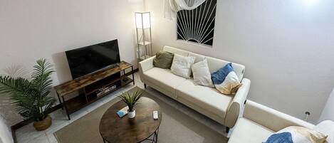 Una sala de estar con televisor, sofá, mesa de centro y una planta en maceta.
