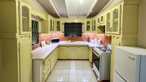 Eine Küche mit hellgrünen Schränken, einer Mikrowelle, einem Gasherd und einem Kühlschrank.