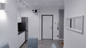 A modern kitchen with a built-in refrigerator, a microwave, and a small countertop. There is a door with a black frame and a window with blinds. - Enjoy your holiday in Naples in this brand new apartment (Napoli)