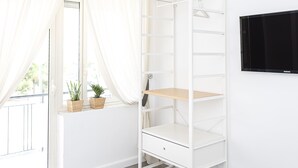 A white room with a built-in white shelving unit, a flat-screen TV on the wall, and a window with white curtains. - Enjoy your holiday in Naples in this brand new apartment (Napoli)