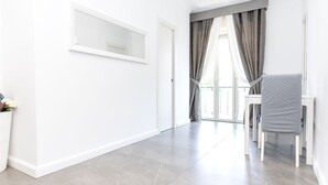 A bright hallway with a white door, a small table with a chair, and a window with curtains. - Enjoy your holiday in Naples in this brand new apartment (Napoli)