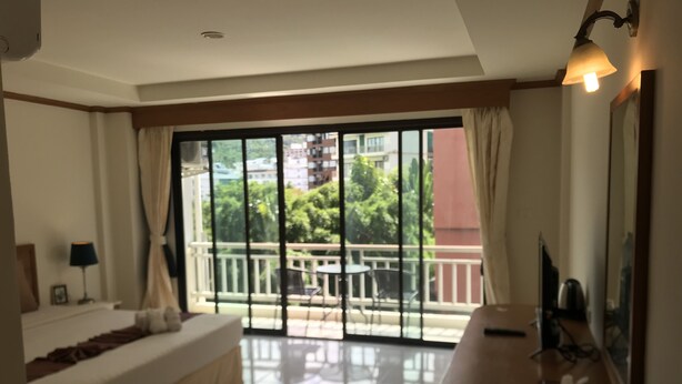 A bedroom with a large sliding glass door leading to a balcony, a bed, a bedside table with a lamp, and a TV on a stand. - Global Hotel Beach View (Patong)