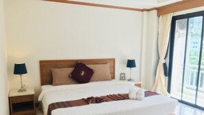 A hotel room with a large bed, two bedside tables with lamps, a wooden headboard, and a view through a large window. - Global Hotel Beach View (Patong)