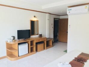 A hotel room with a wooden entertainment unit, a flat-screen TV, a small refrigerator, a mirror, and a wall-mounted air conditioner. - Global Hotel Beach View (Patong)