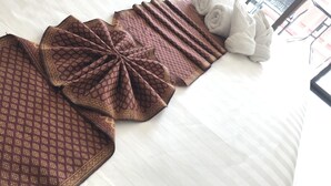 A neatly made bed with a patterned blanket, rolled towels, and a view of the outside through a window. - Global Hotel Beach View (Patong)