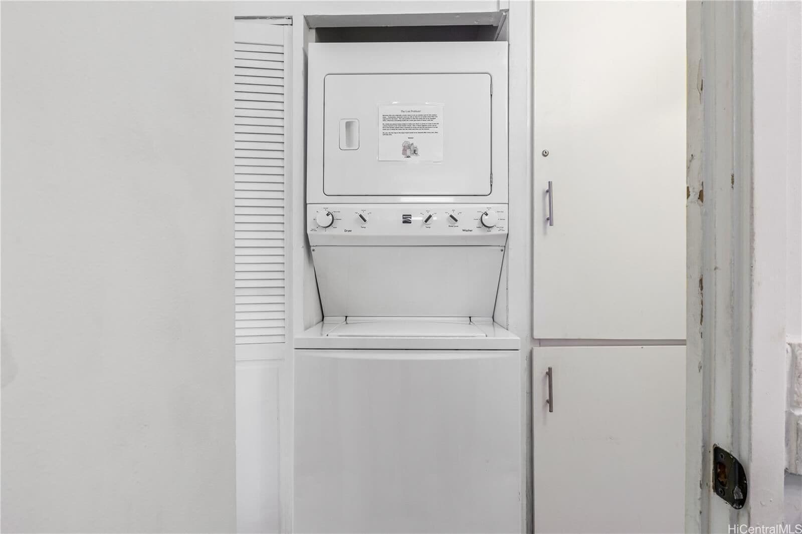 Ein weißer Hauswirtschaftsraum mit einem großen weißen Gerät, vermutlich einer Waschmaschine und einem Trockner, und einer Tür mit Griff.