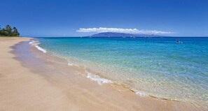 Una playa con agua turquesa cristalina, una orilla de arena y una montaña distante.